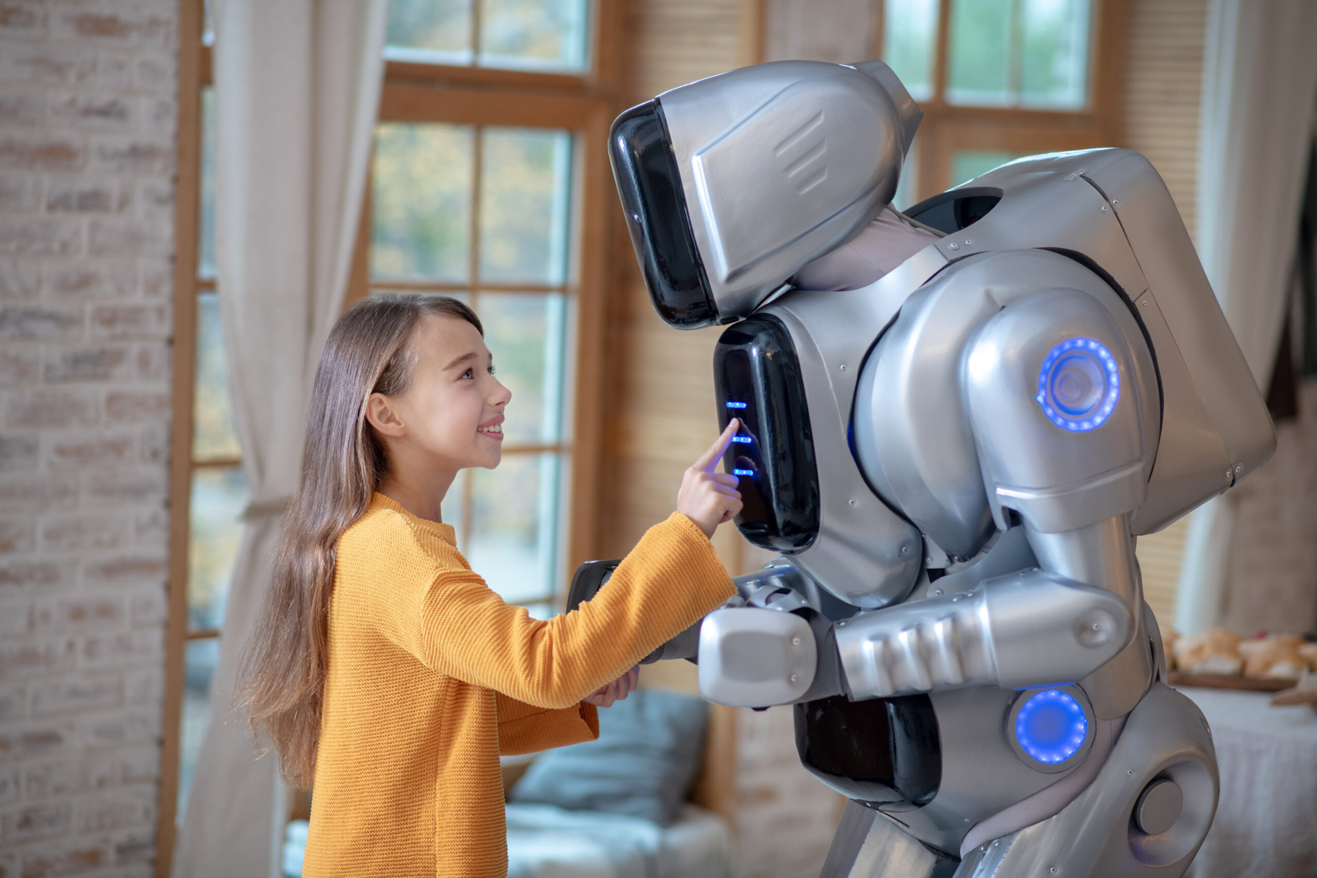House helper. Girl in orange shirt standing near house robot while setting the program